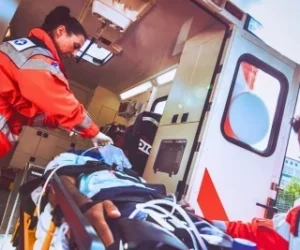 Two paramedics loading an injured man on a stretcher into an ambulance after a catastrophic injury.